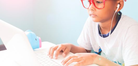 Little boy child wearing red glasses listening and using laptop computer