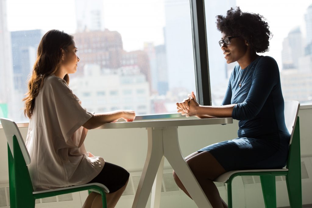 Two women sitting across from each other at a table by a window