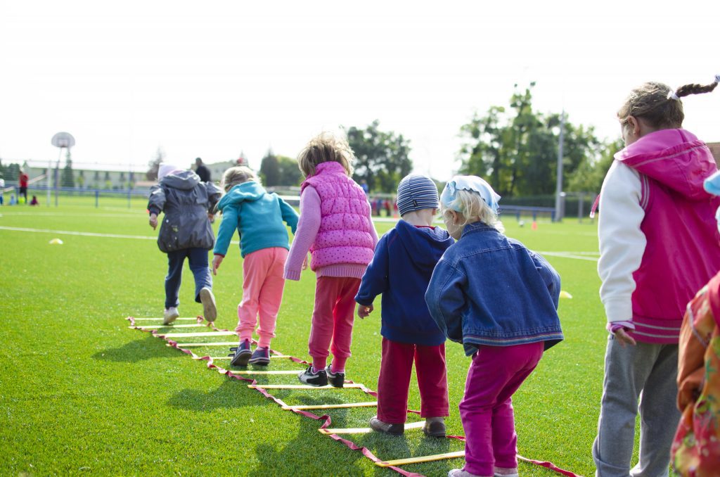 Kids in a line engaging in a jumping competition outside