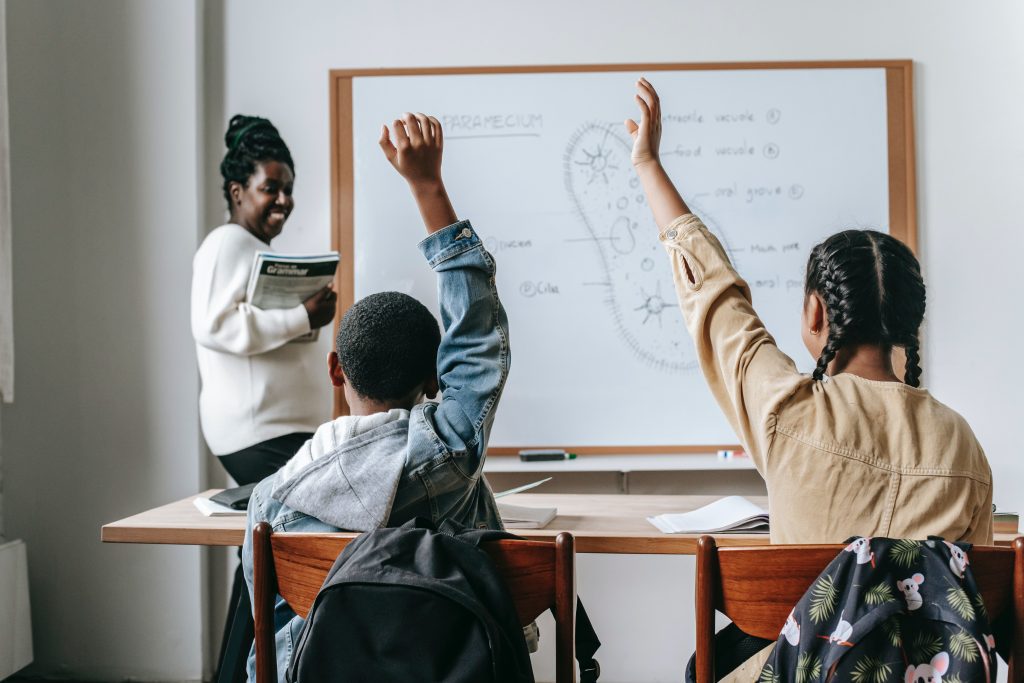 Teacher smiling as students raise their hands