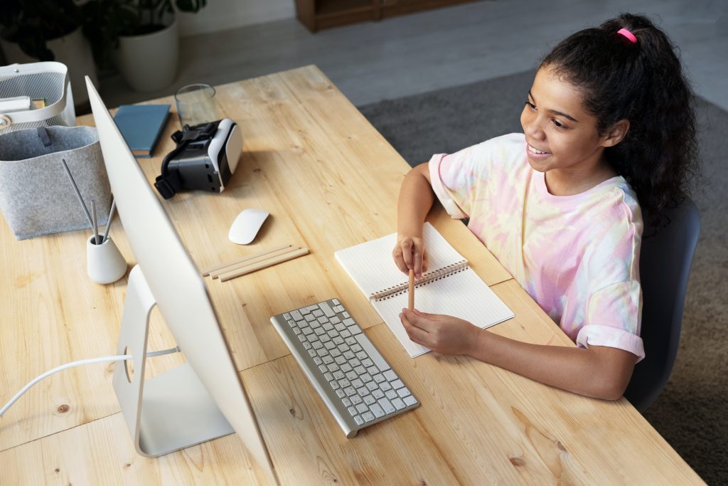 A student wearing a pink tie-dye t-shirt smiles while looking at a computer screen