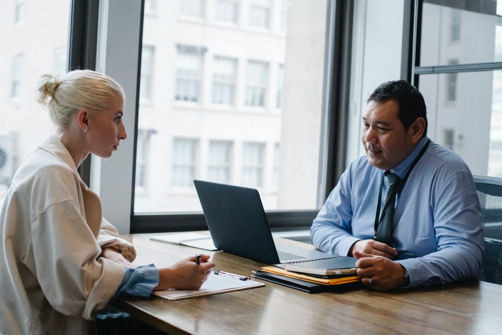 A man and a woman engaged in conversation sitting across a desk from each other