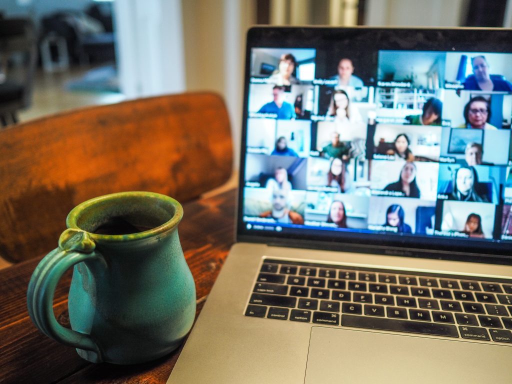 Laptop displaying group of people in grid view during a Zoom meeting, with a coffee mug sitting on the table nearby.