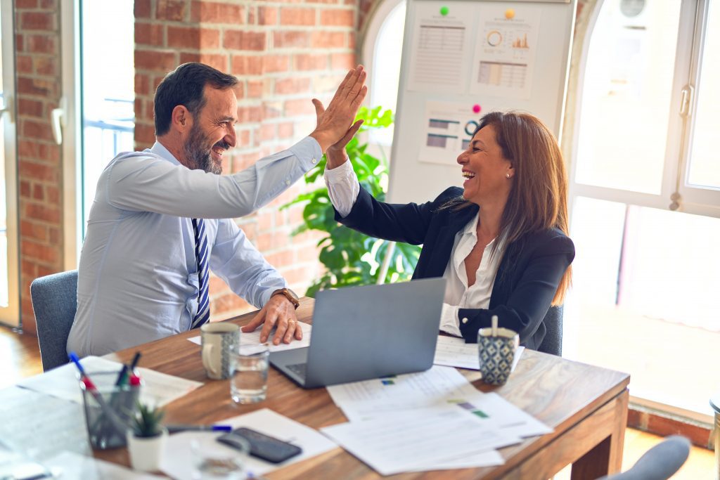 Man and woman high five while sitting at a table with papers spread in front of them