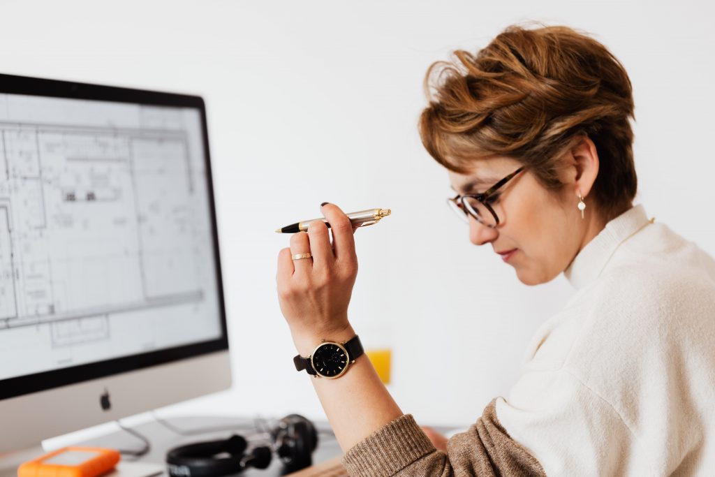 Woman sitting at desk in front of computer with pen in hand thinking