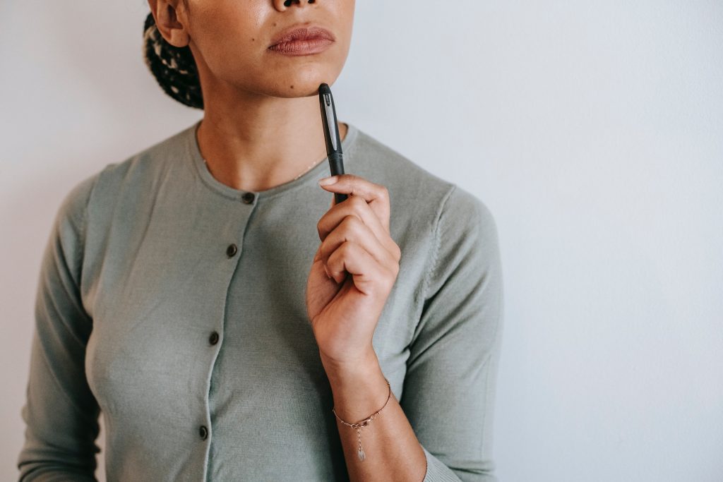 Pensive woman standing wtih pen to her chin