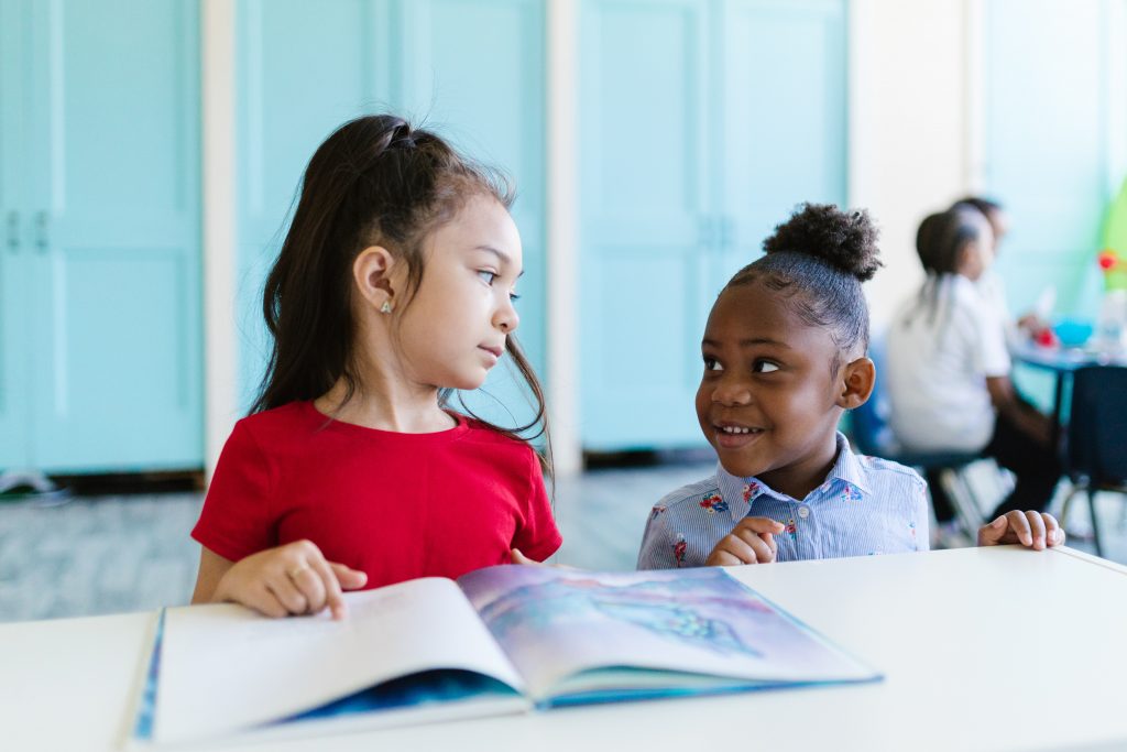 Two girls sitting at a table sharing a book