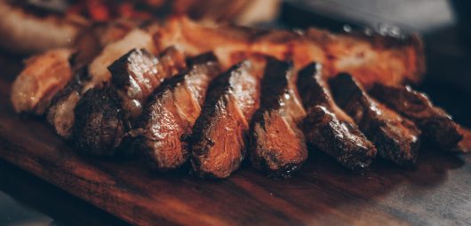 Cooked sliced meat situated on a dark cutting board
