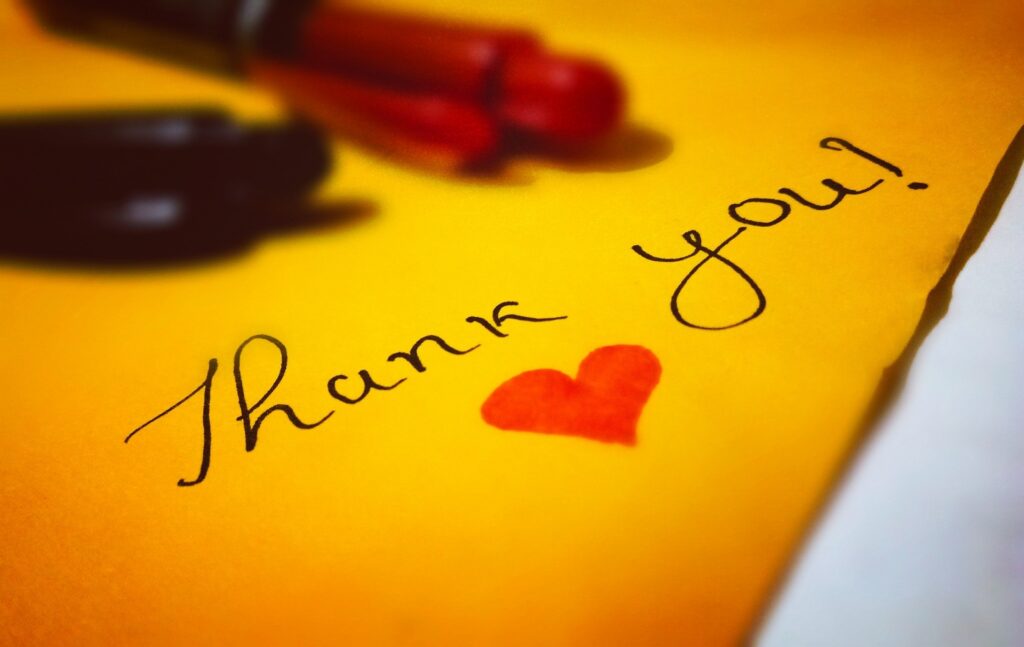 The words thank you written on a yellow paper with a red heart colored in